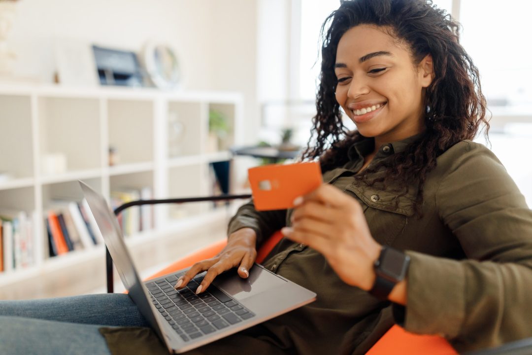 Happy woman holding debit credit card, using pc