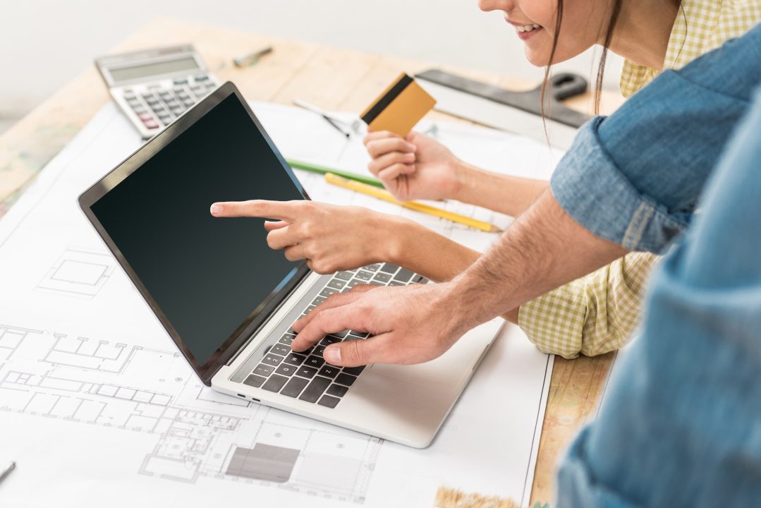cropped shot of couple with credit card using laptop with blank screen during renovation