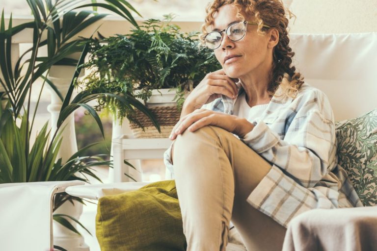 Woman portrait sitting on a chair at the garden at home thinking about her savings.