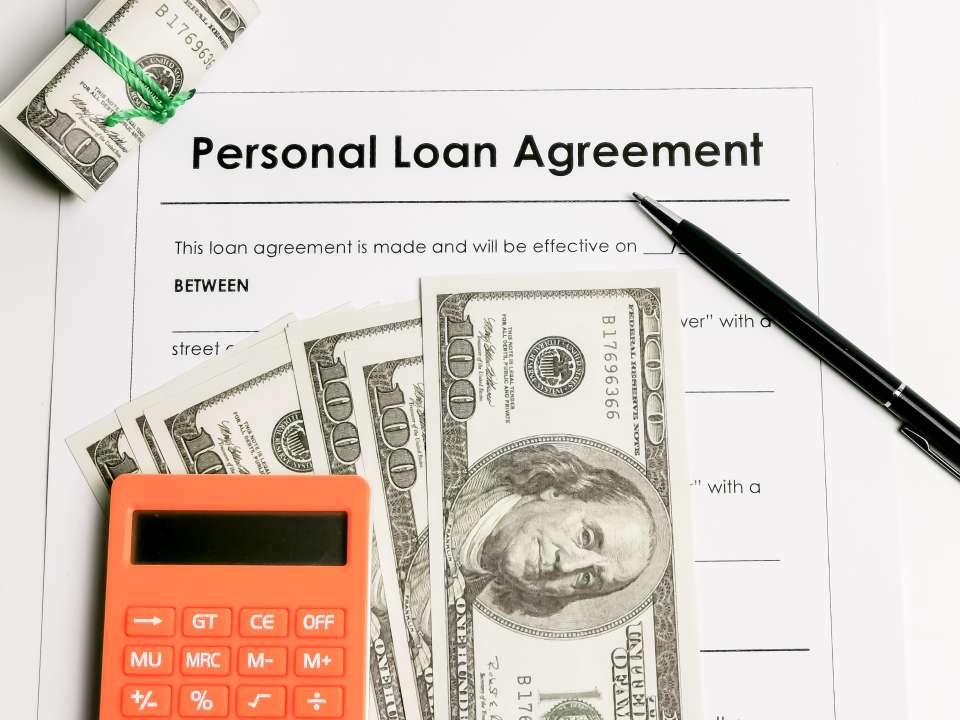 Filling up personal loan agreement form with a pen, calculator and fake money.